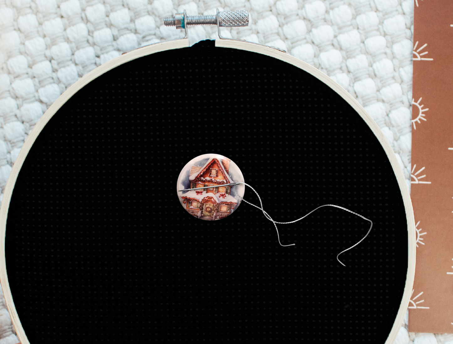 Round magnetic needle minder showing a snowy gingerbread house with holiday garland and bows